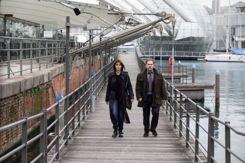 Petra Delicato (Paola Cortellesi) und Antonio Monte (Andrea Pennacchi) gehen am Hafen in Genua zu ihrem Stammcafé. 