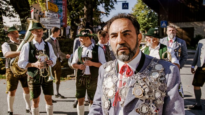 Schützenkönig Toni Freitag (Adnan Maral) will ins Bürgermeisteramt. Auf dem Weg dorthin dirigiert er erstmal die Blaskapelle.
