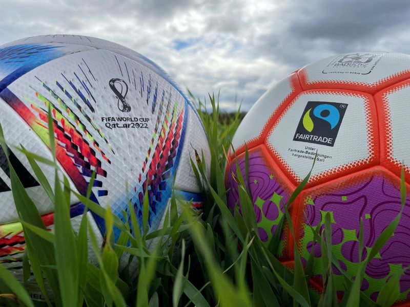 Auf einem Ball prangt das Fairtrade-Abzeichen, auf dem anderen das Logo der Fußball-WM in Katar. Sind die Nachhaltigkeits-Kampagnen großer Sportartikelhersteller mehr Schein als Sein?