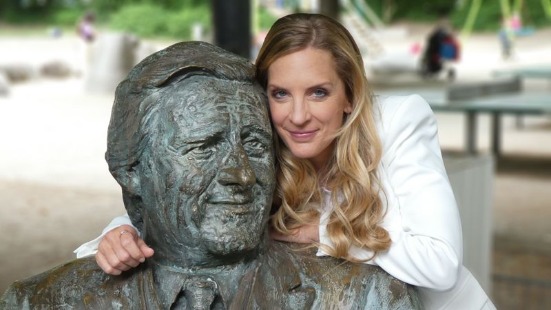 Erinnerungen an ein Original des Fernsehens und der Stadt München: Moderatorin Caro Matzko am Denkmal für Helmut Fischer als Monaco Franze vor dem Café "Münchner Freiheit".