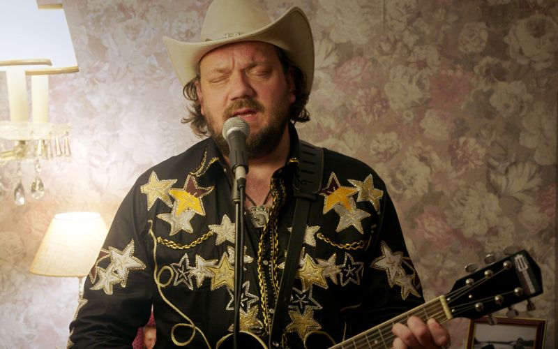 Der abgehalfterte Country-Schlagerstar Jeff Kanter (Charly Hübner) spielt in David Schalkos Anthologie-Serie "Warum ich?" Wohnzimmerkonzerte bei fremden Leuten. Dabei hat er in der Episode "Cowboys" eine verstörende Begegnung.