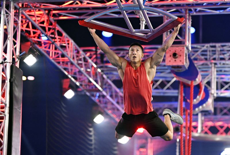 Dieses Hindernis, an dem sich hier David Wollschläger abmüht, heißt "Buschis Rache". Es ist ein Denkmal für Frank Buschmann, der seine letzte Staffel als Moderator von "Ninja Warrior Germany" (RTL) bestreitet. Zur Einweihung gibt's Schampus-Dusche. Buschi ist gerührt: "Das geht unter die Haut." Dann feixt er: "Da fliegt ihr alle rein, ihr Pflaumen."