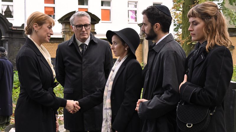 Oberstaatsanwältin Scheffer (Helene Grass, links), die Nachfolgerin des Ermordeten Frank Leuw, besucht mit Polizeichef Wenzel (Max Urlacher, zweiter von links) Leuws Beerdigung. Die Witwe Ruth (Sharon Brauner, Mitte), der Rabbiner Samuel (Garry Fischmann), ein enger Freund der Leuws, und seine Frau Hannah (Morgane Ferru) sind ebenfalls anwesend. 