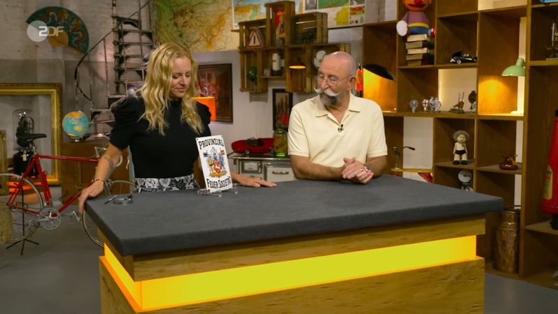 "Ich mag alte Werbeschilder", erklärte Horst Lichter angesichts des bunten Verkaufsobjekts. Annika Raßbach lächelte voller Vorfreude, denn sie wusste, dass sie den Moderator mit Fachwissen verblüffen würde ...