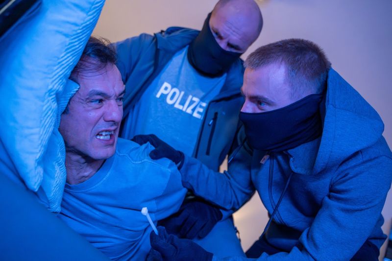 Ein Mann schläft auf dem Sofa ein. Als er aufwacht, stehen zwei falsche Polizisten vor ihm.