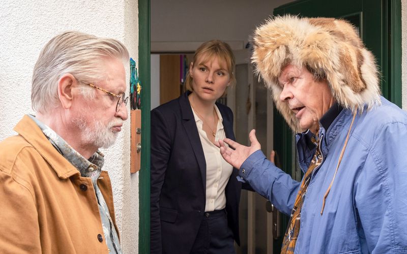 Der alte Griesgram (Heikki Kinnunen, rechts) drängt seinen Bruder Tarmo (Kari Väänänen), auf dem Weg zu dem roten Escort einen Zwischenstopp bei Tarmos entfremdeter Tochter Maria (Rosalie Thomass) einzulegen. 